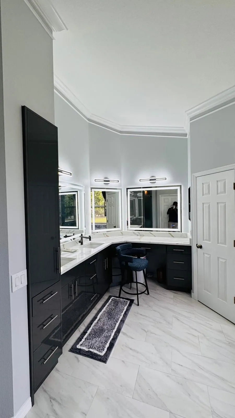 Black high-gloss corner vanity with a makeup station and lit mirrors